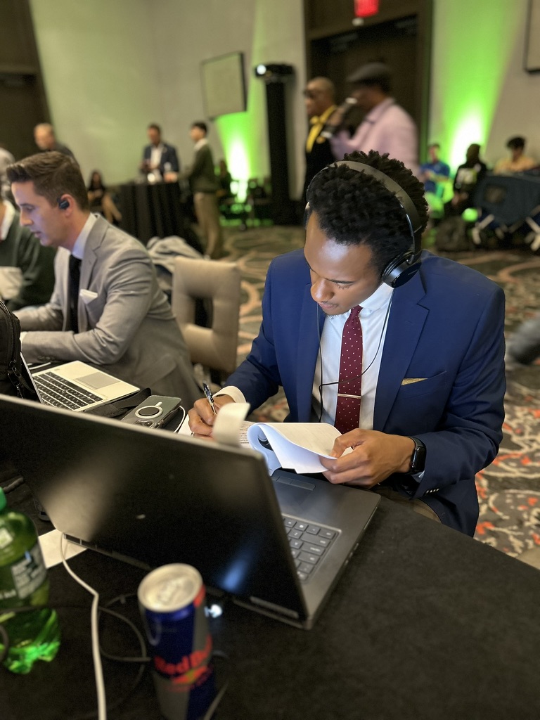 Stephon Dingle reviews notes at a laptop while wearing broadcast headphones.