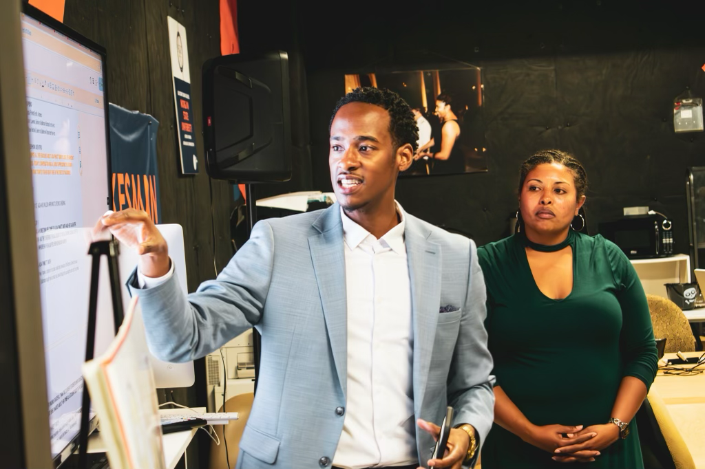 Stephon Dingle guides a colleague through work displayed on a newsroom monitor.