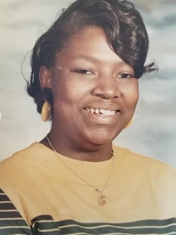 A younger Ms. Sheila Plato smiling outdoors in a white blouse.