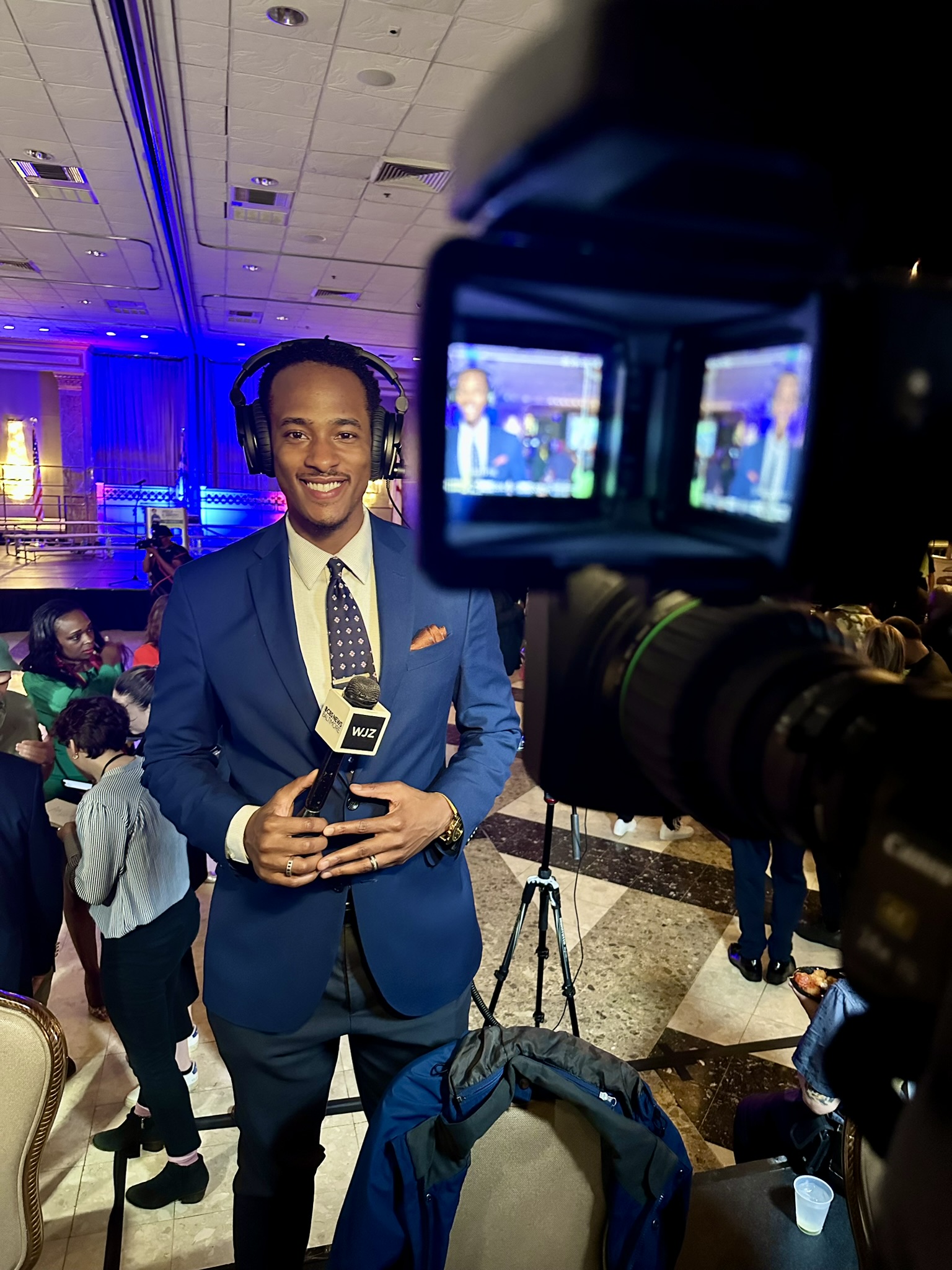 Stephon Dingle reporting for WJZ while wearing headphones and holding a microphone.