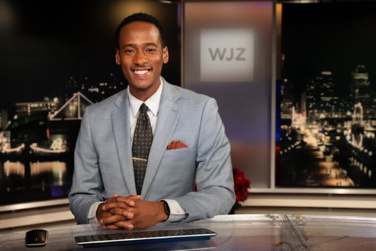 Stephon Dingle seated at the WJZ anchor desk with Baltimore’s skyline behind him.